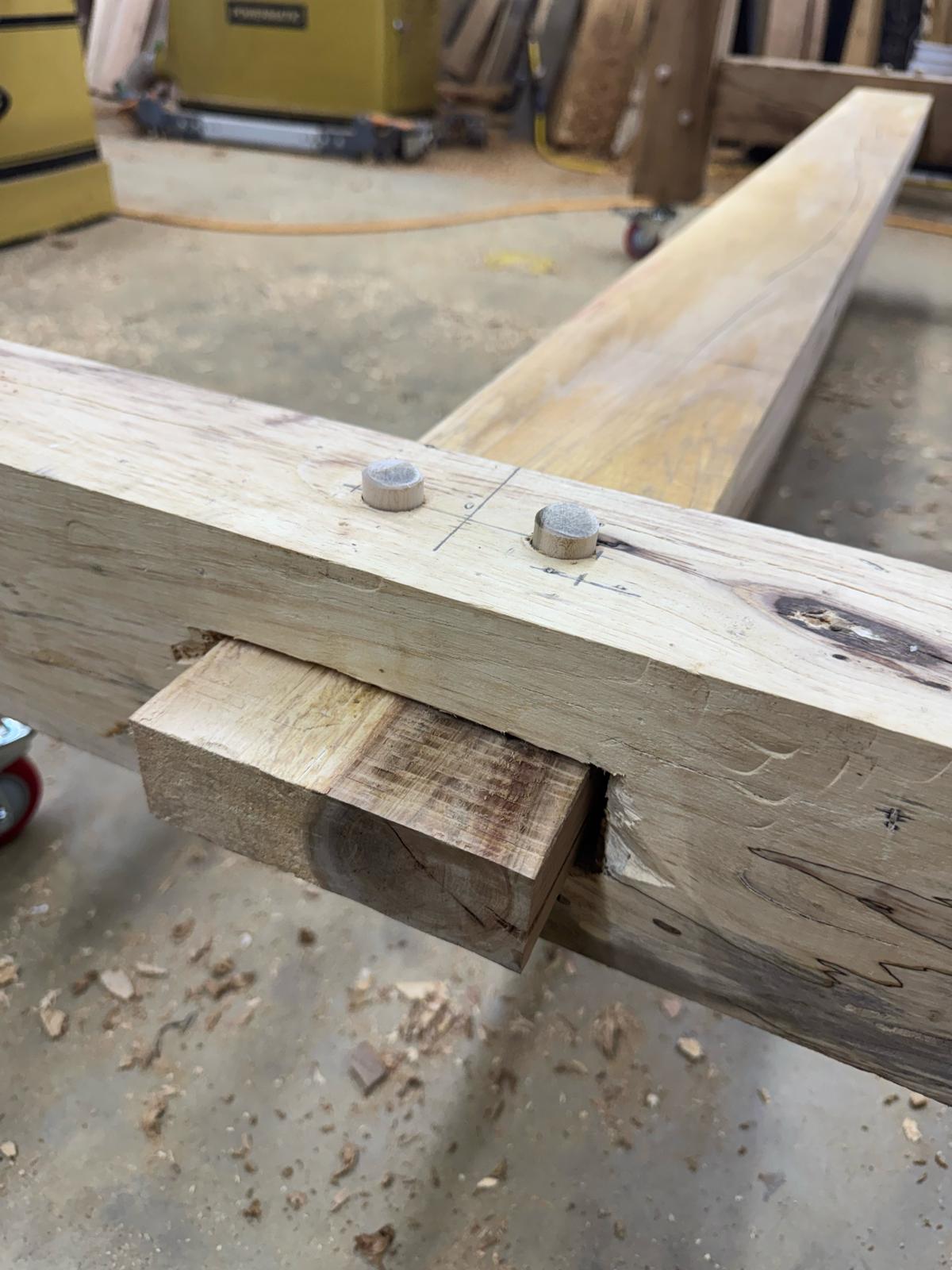 Two rough timbers fitted together with a joint on the shop floor, with wood chips around
